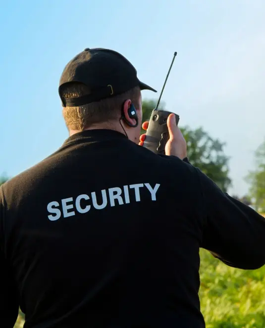 A security guard is holding a walkie talkie.